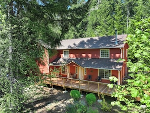 Casa roja de dos pisos con un porche de madera, rodeada de un bosque denso.