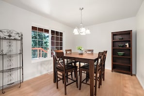 Un comedor con mesa de madera, sillas, una lámpara de araña, una ventana con vistas y una estantería.