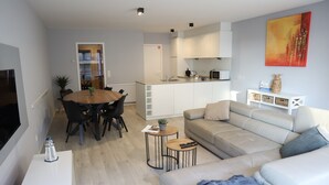 Ett modernt vardagsrum med en soffa, ett matbord med stolar, en tv och ett köksområde med skåp och en mikrovågsugn.