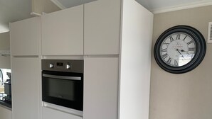 A kitchen with white cabinets, a built-in oven, and a wall clock. - Wonderful Holiday Home in Nieuwpoort Near Dunepark (Nieuwpoort)
