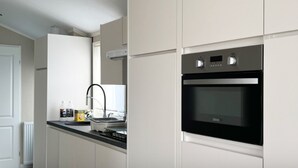 A modern kitchen with white cabinetry, a built-in oven, and a stainless steel range hood. - Wonderful Holiday Home in Nieuwpoort Near Dunepark (Nieuwpoort)