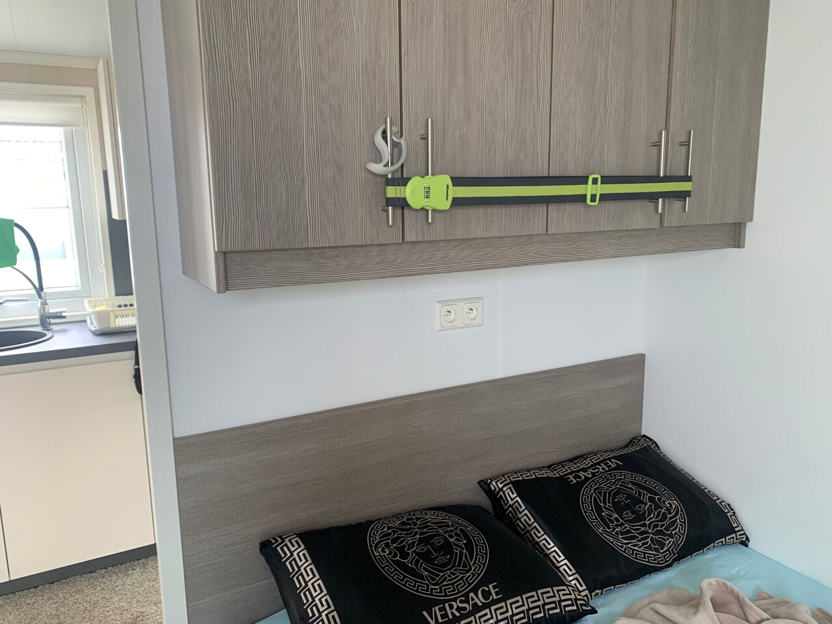 Un dormitorio con cabecera de madera, una cama con dos almohadas negras de diseño geométrico y una toalla verde a rayas colgada de un perchero.