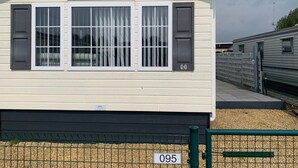 A single-story mobile home with a gabled roof, two large windows with shutters, and a small porch area. - Wonderful Holiday Home in Nieuwpoort Near Dunepark (Nieuwpoort)