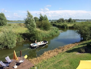 A river with a boat, surrounded by greenery and a grassy area with a deck and chairs. - Beachvilla Ijsselmeerblik (Makkum)