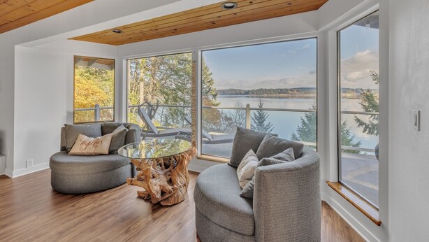 Ein modernes Wohnzimmer mit Holzbalkendecke, großen Fenstern und Blick auf einen See.