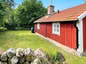 A red wooden house with a tiled roof, a chimney, and a stone wall in the foreground. - 4 Person Holiday Home in Farjestaden (Farjestaden)