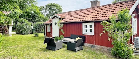 Una casa de madera roja con techo de tejas, un pequeño porche con banco y un jardín.