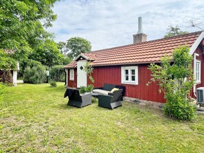 Une maison en bois rouge avec un toit en tuiles, un petit porche avec un banc et un jardin.