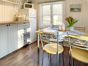 A kitchen with white cabinets, a wooden countertop, a round dining table with chairs, and a window with a view of trees. - 4 Person Holiday Home in Farjestaden (Farjestaden)