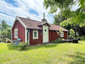 A red wooden house with a white door, a chimney, and a small porch with blue chairs. - 4 Person Holiday Home in Farjestaden (Farjestaden)