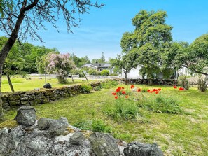 A stone wall, a grassy area with red flowers, and a white building with a dark roof. - 4 Person Holiday Home in Farjestaden (Farjestaden)