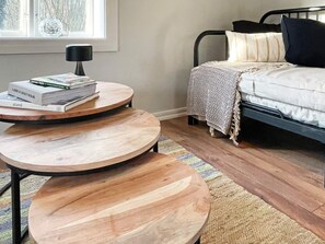 A bedroom with a bed, a bedside table with books, a round wooden table, and a window with a view of trees. - 4 Person Holiday Home in Farjestaden (Farjestaden)