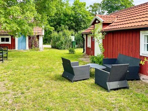 En rødmalede træbygning med tegltag, græsplæne og udendørs møbler.