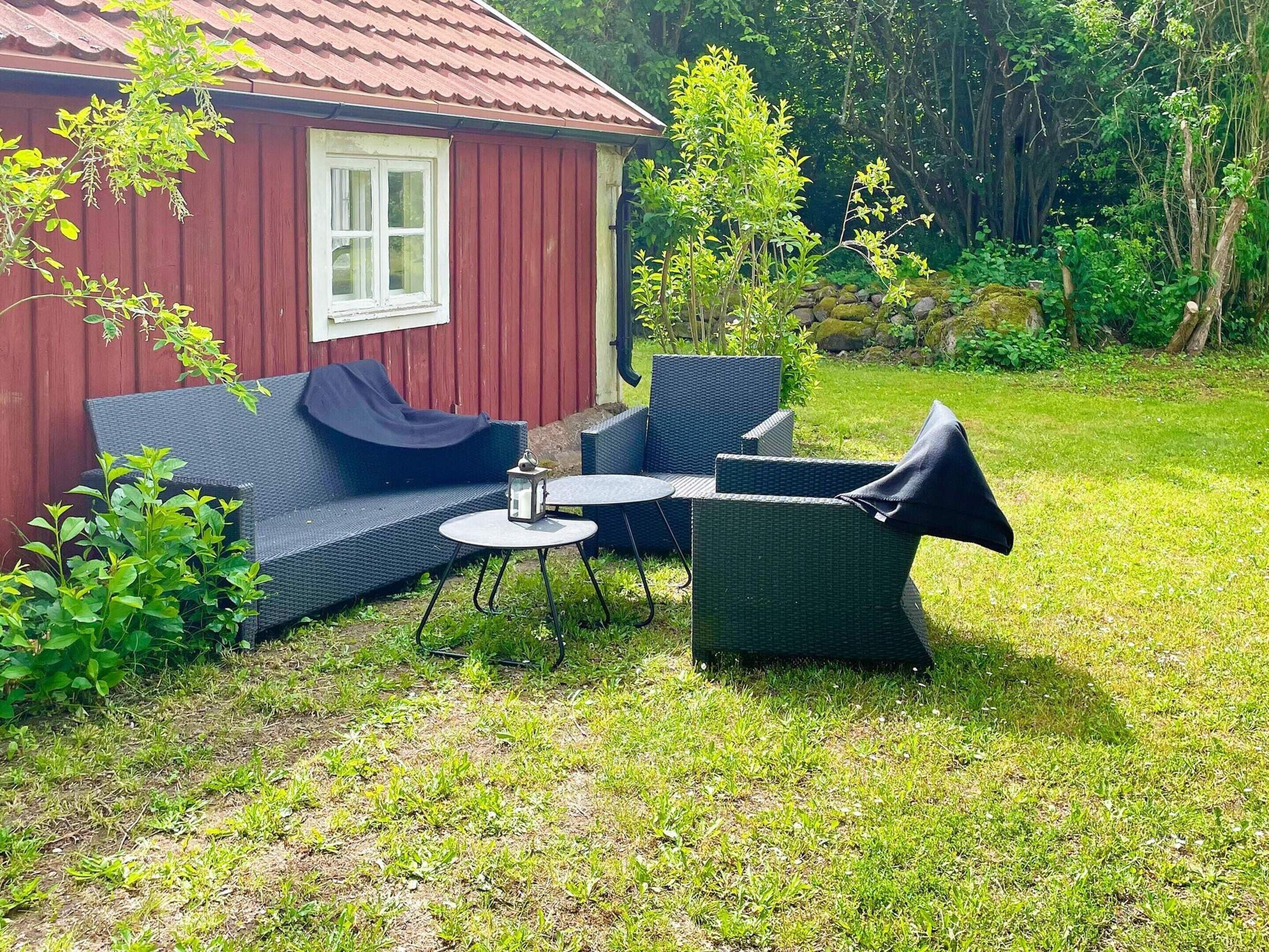 A red wooden house with a white window, a blue sofa, and a round table with chairs in a grassy backyard.