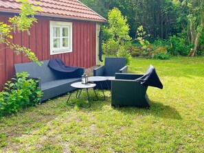 A red wooden house with a white window, a blue sofa, and a round table with chairs in a grassy backyard. - 4 Person Holiday Home in Farjestaden (Farjestaden)