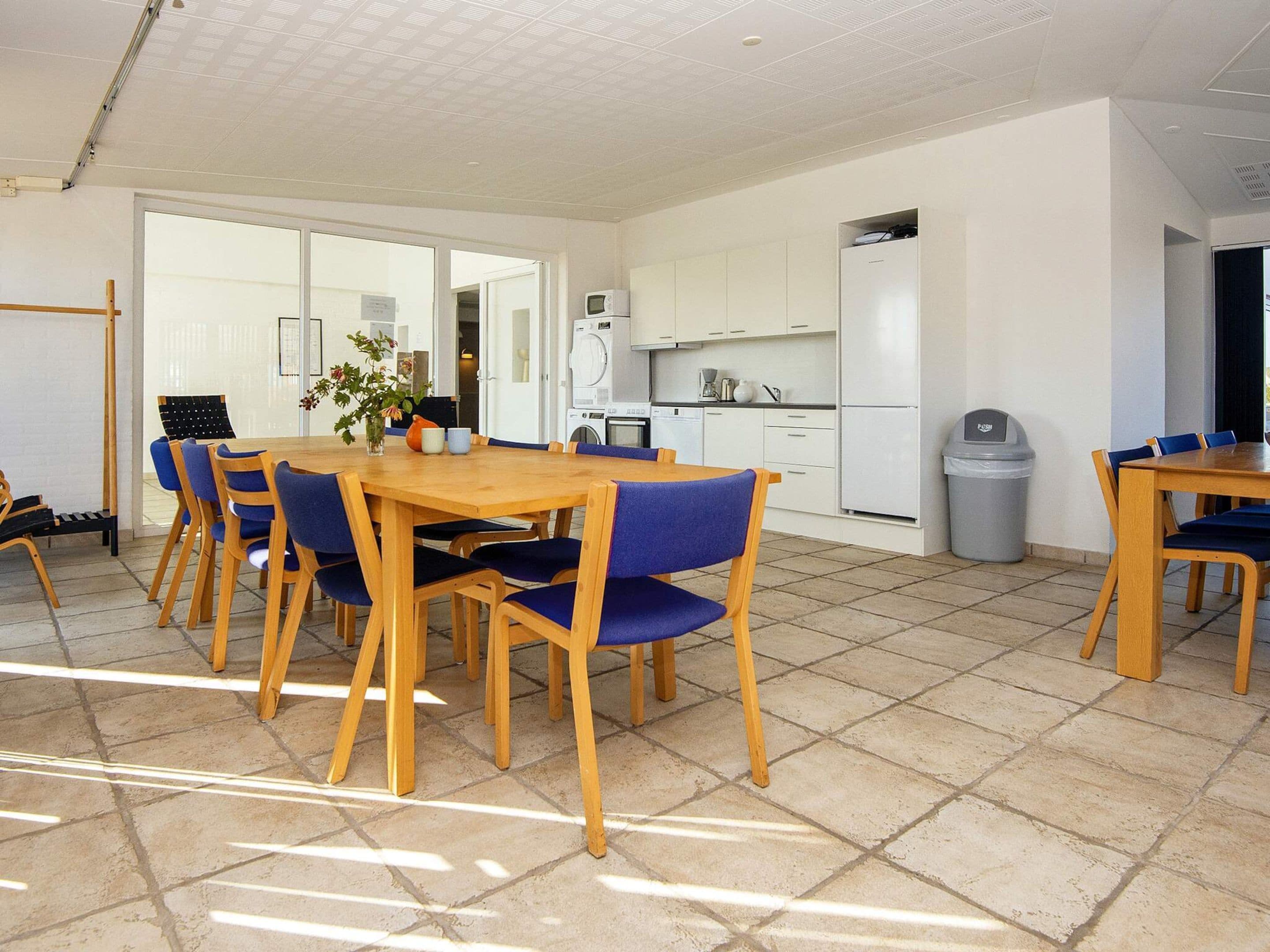 Una cocina moderna con gabinetes blancos, un microondas y un refrigerador. Hay una zona de comedor con una mesa de madera y sillas azules.