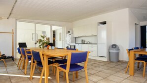 Una cocina moderna con gabinetes blancos, un microondas y un refrigerador. Hay una zona de comedor con una mesa de madera y sillas azules.
