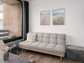 A modern living room with a grey sofa, a small table with a vase, and two framed beach pictures on the wall.