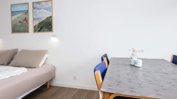 Een kamer met een bed, een eettafel met stoelen en twee afbeeldingen in lijsten aan de muur.