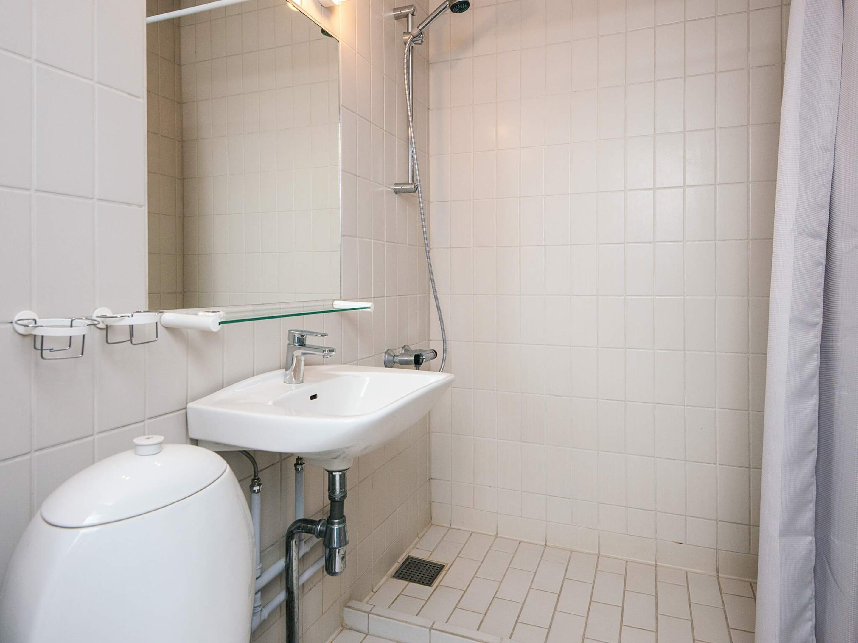 Un baño con un lavamanos blanco, un estante de vidrio, una ducha y un inodoro.