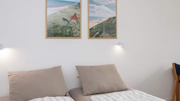 Un dormitorio con dos camas, vista a la playa y dos cuadros en la pared.