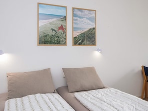 A bedroom with two beds, a view of the beach, and two framed pictures on the wall. - 3 Person Holiday Park Home in Ulfborg (Ulfborg)