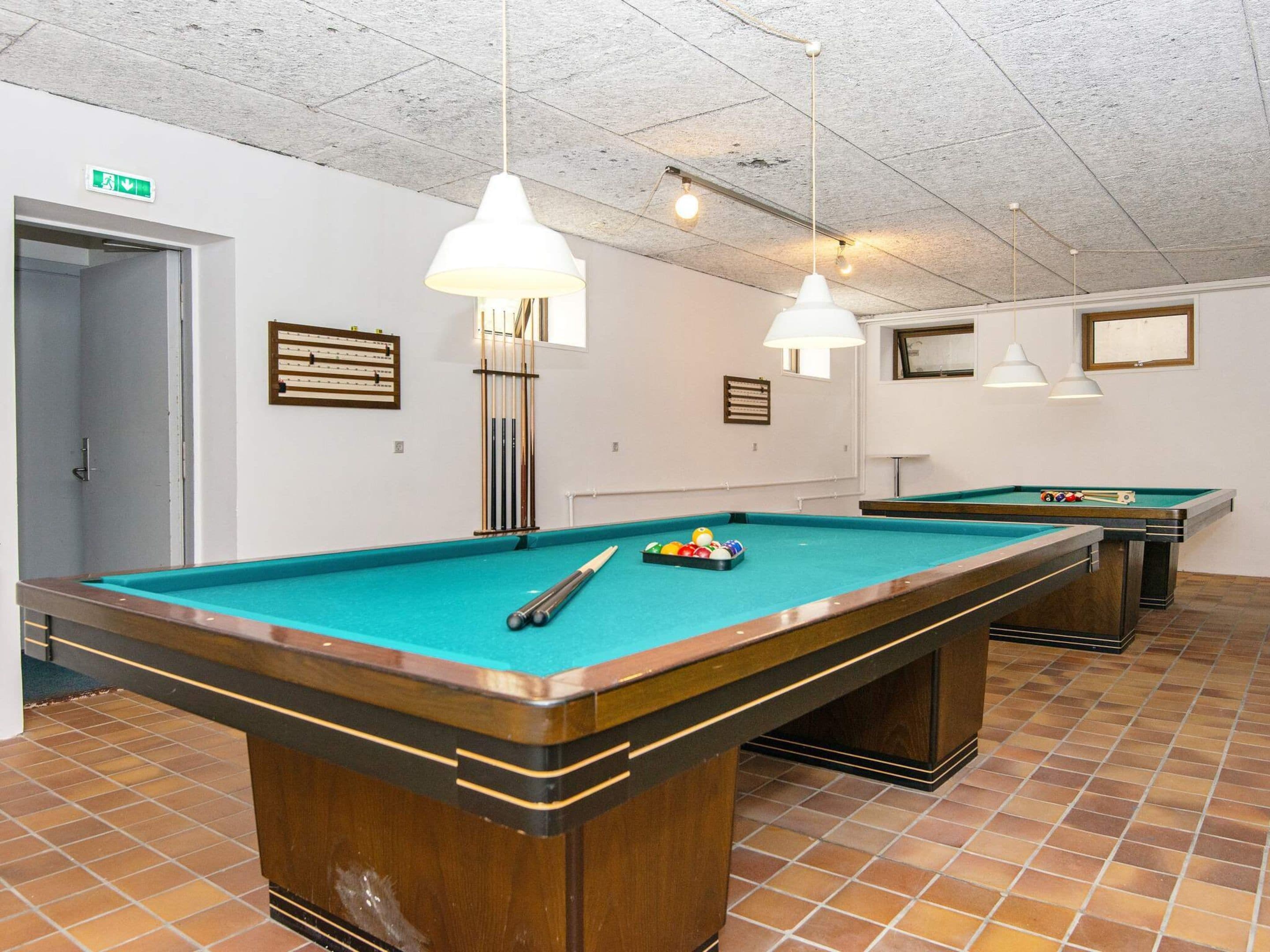 A pool table with a cue stick and balls, a second table in the background, and a ceiling with hanging lights.