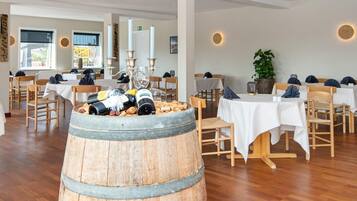 A restaurant with wooden flooring, white tables, and chairs. There is a barrel with wine bottles and corks.