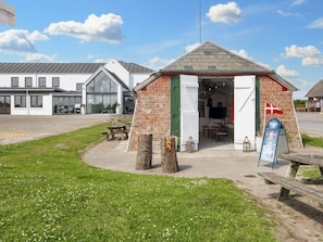 A small brick building with a green door and a flag, a picnic table, and a signboard. - 3 Person Holiday Park Home in Ulfborg (Ulfborg)