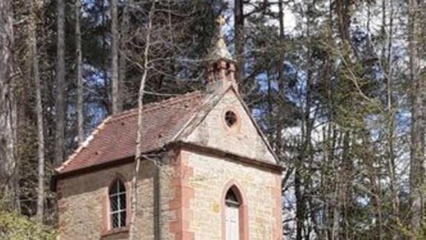 A small stone chapel with a pitched roof, arched entrance, and a bell tower, surrounded by a grassy area and trees. - Holiday Apartment Wine bar (Königheim)