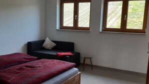 A bedroom with a bed, a sofa, and two windows with a view of greenery. - Holiday Apartment Wine bar (Königheim)