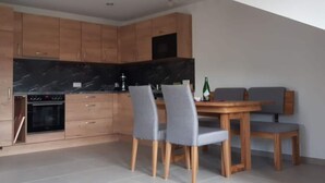 A modern kitchen with wooden cabinets, a black marble countertop, and a dining area with grey chairs and a wooden table. - Holiday Apartment Wine bar (Königheim)