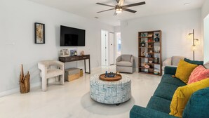 A living room with a round coffee table, a sofa, a television, a bookshelf, and a ceiling fan. - Relax N Rentals Waterfront 4BR 2BA Port Charlotte FL Pool Kayaks Harbor Access (Port Charlotte)