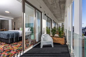 A modern hotel room with a large bed, a glass door leading to a balcony, and a view of the city.