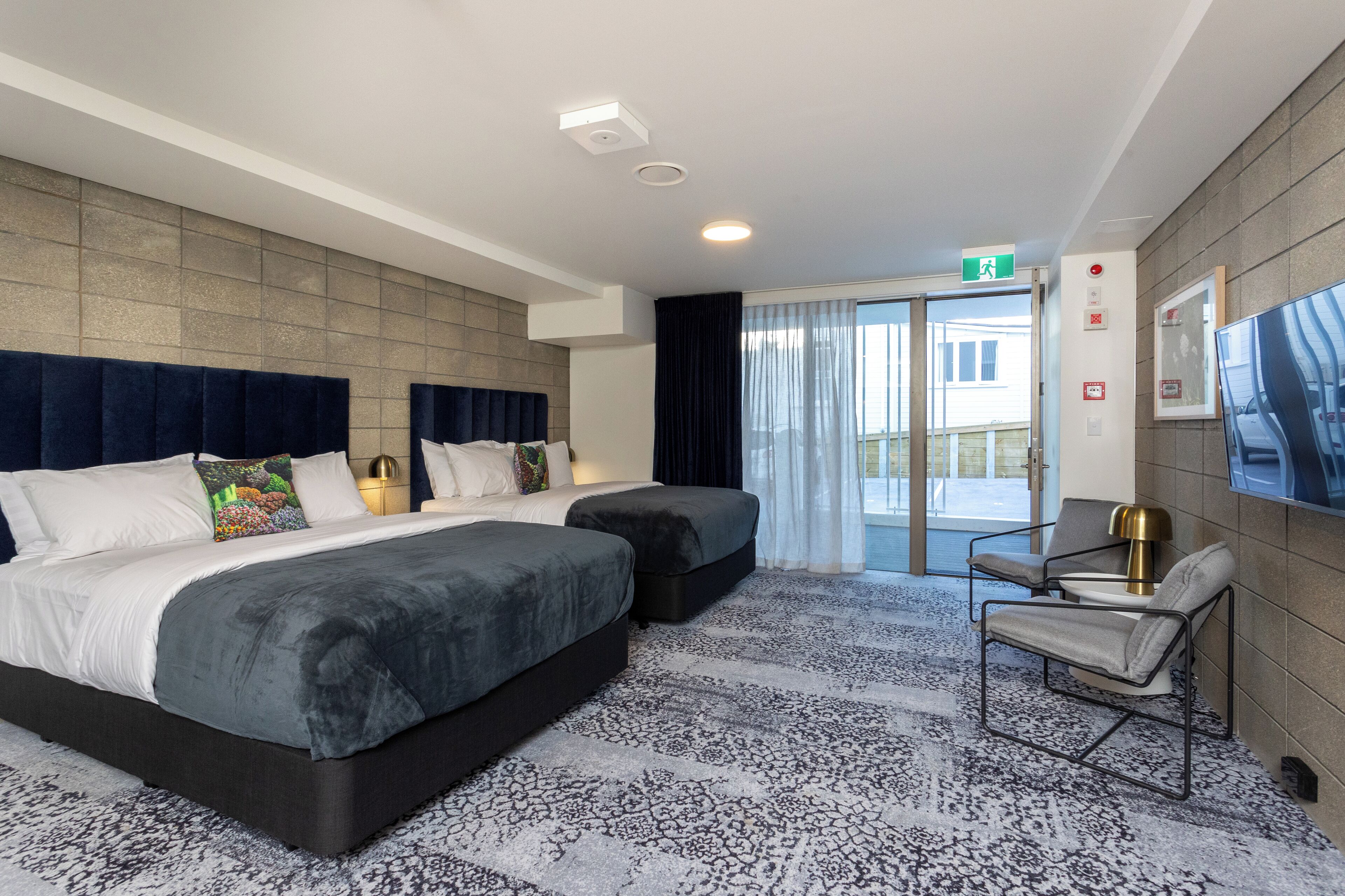 A hotel room with a large bed, two bedside tables, a chair, a TV, and a view of the outside.