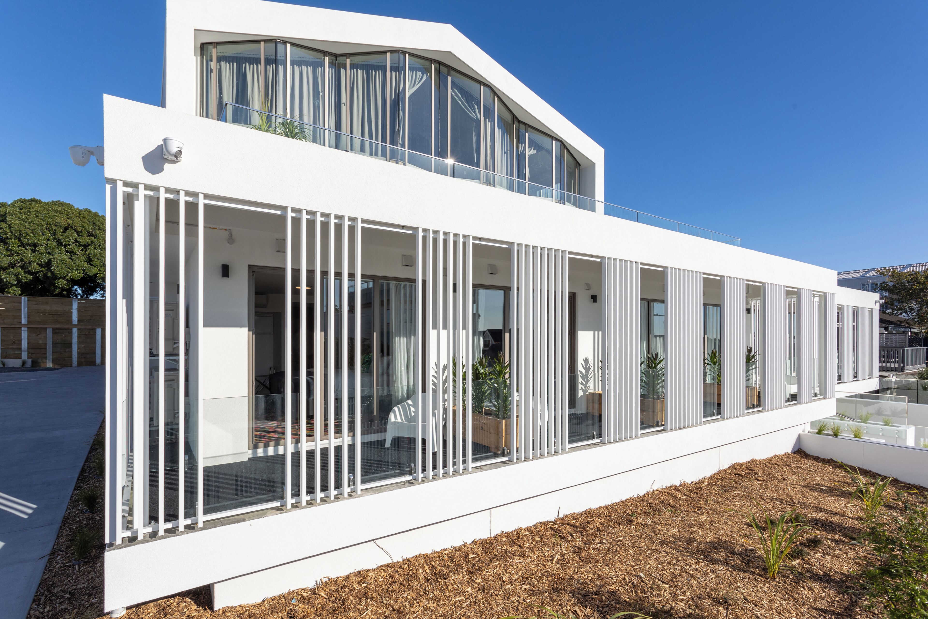 Un edificio moderno con fachada blanca, ventanas grandes y un balcón con plantas.