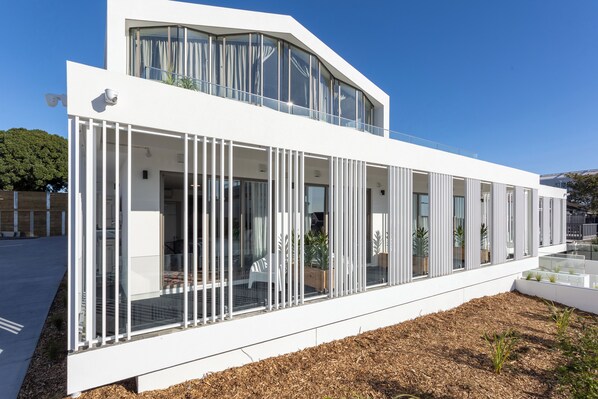 A modern building with a white exterior, large windows, and a balcony with plants.