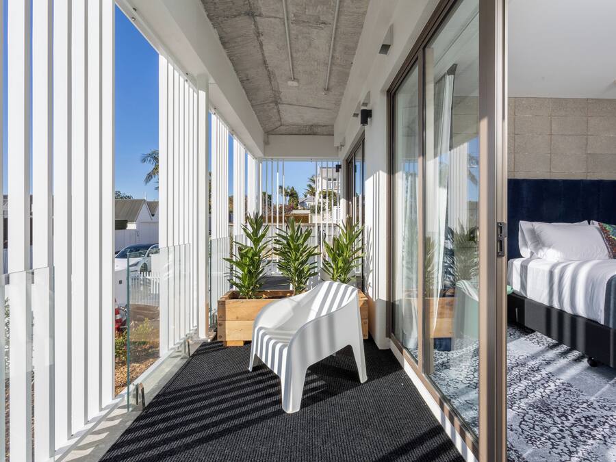 A balcony with a bed, a white chair, and potted plants.