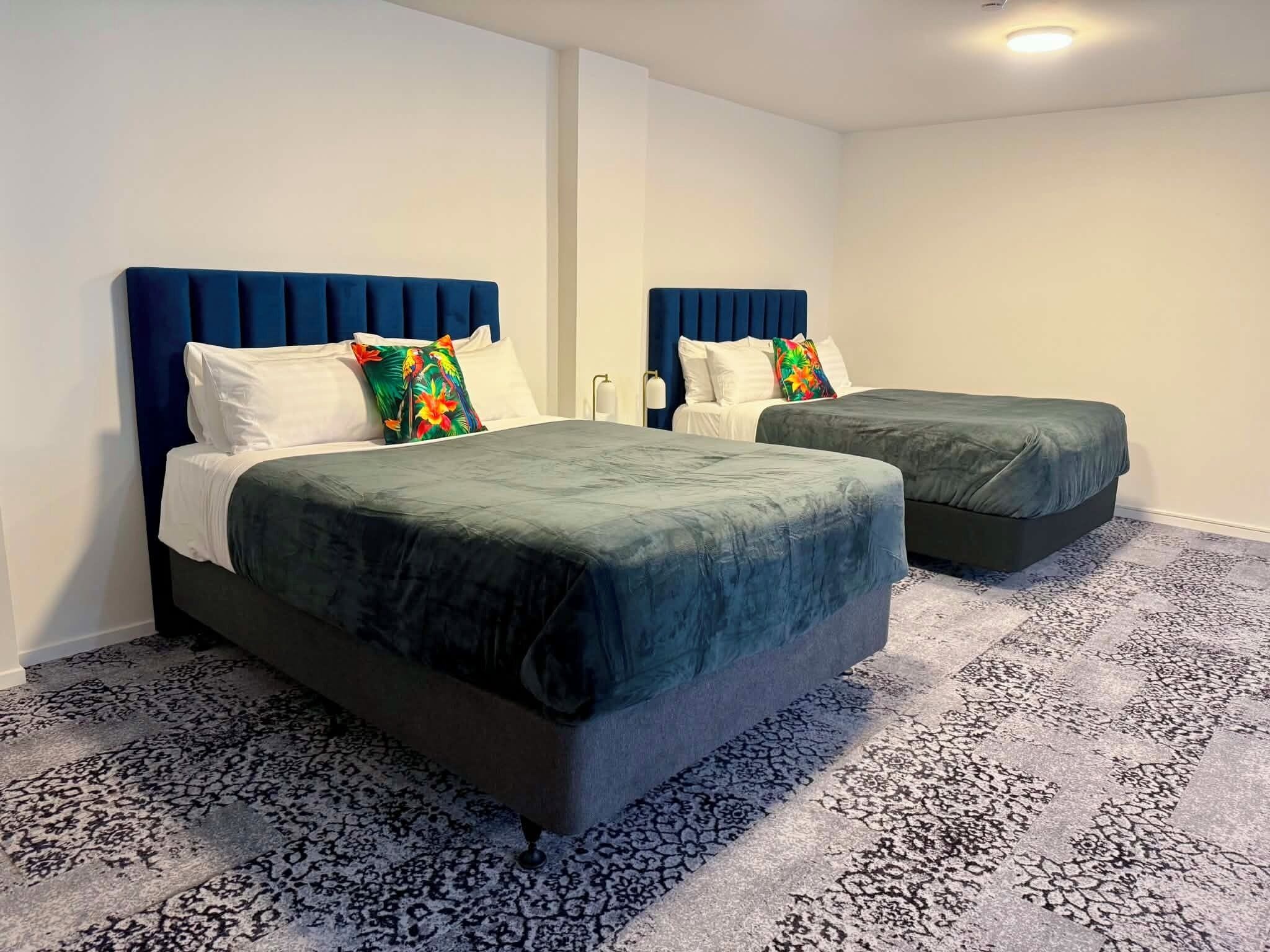 A hotel room with two beds, each with a blue headboard, white bedding, and a patterned carpet.