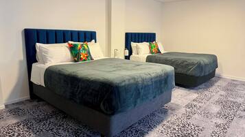 A hotel room with two beds, each with a blue headboard, white bedding, and a patterned carpet.
