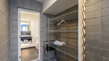 A modern bathroom with grey tiled walls, a white door leading to a bathroom area, and metal shelves with a towel rack.