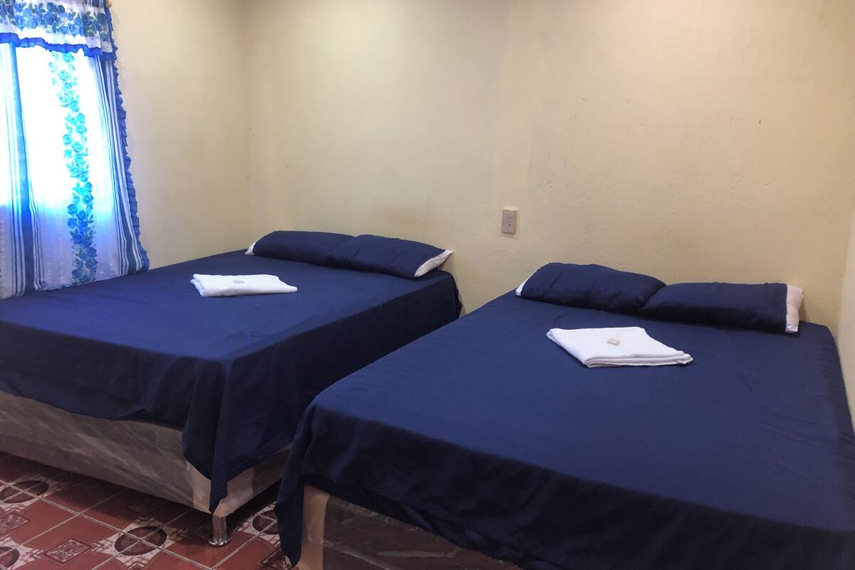 Two single beds with dark blue bedding and white towels, a patterned tiled floor, and a window with blue curtains.