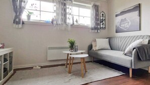 A living room with a grey sofa, a small round table with a plant, a radiator, and a window with curtains. - 8 Person Holiday Home in Masfjordnes (Masfjorden)