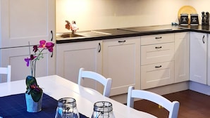 A modern kitchen with white cabinets, a black countertop, and a dining table with chairs. There are two glass jars on the table and a potted orchid. - 8 Person Holiday Home in Masfjordnes (Masfjorden)