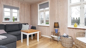 A cozy room with a grey sofa, a small white table, wicker chairs, and a window with a view. - 4 Star Holiday Home in Grenaa (Grenaa)