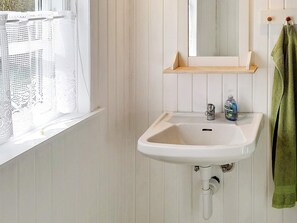 A bathroom with a white sink, a mirror, a window with a white curtain, and a green towel hanging on a hook. - 4 Star Holiday Home in Grenaa (Grenaa)