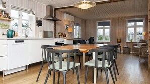A modern kitchen with wooden cabinets, a central island, and a dining area with a wooden table and chairs. - 4 Star Holiday Home in Grenaa (Grenaa)