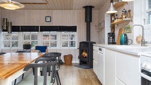 A modern kitchen with a central island, white cabinetry, a stove, and a window overlooking a forested area. - 4 Star Holiday Home in Grenaa (Grenaa)