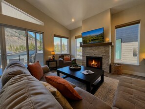 A living room with a fireplace, a sofa, a coffee table, and a television mounted above the fireplace.