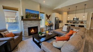 Ein modernes Wohnzimmer mit Kamin, einer Couch, einem Couchtisch und einer Küche im Hintergrund.